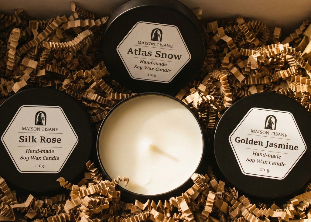Three candles with labels 'Silk Rose', 'Atlas Snow', and 'Golden Jasmine' on a bed of decorative paper.